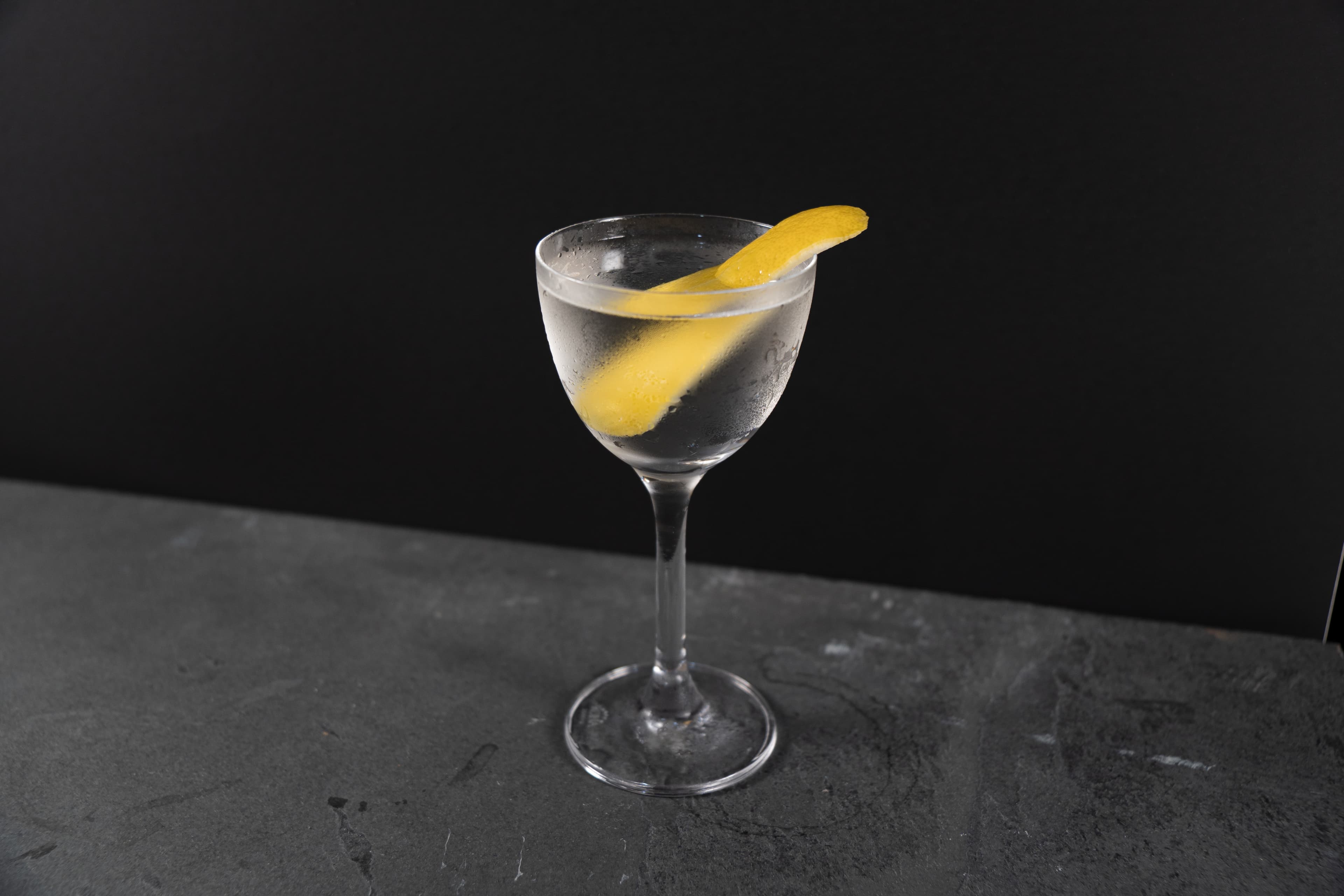 A martini glass with a citrus garnish on a dark bar surface